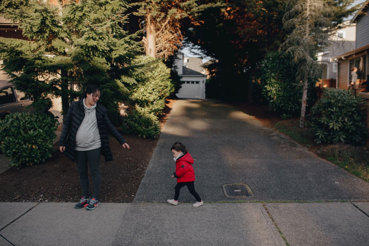 A mother heading out the door with her toddler in a red coat
