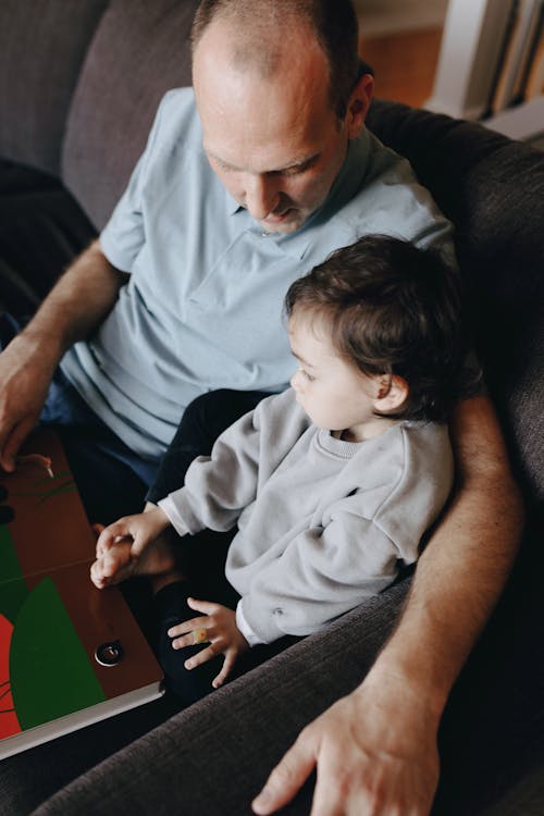 Free Father Holding A Book Beside His Child Stock Photo