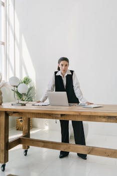 Professional woman standing at a wooden desk in a bright, modern office setting.