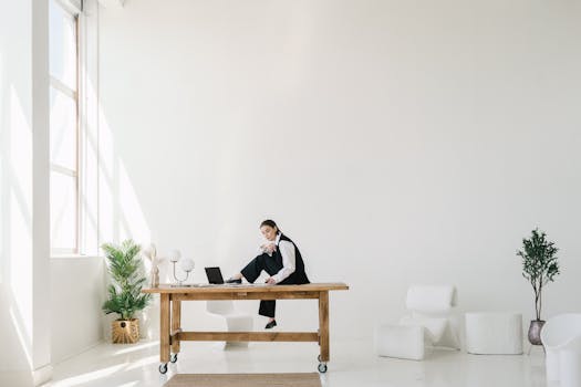 Elegant minimalist office with a woman in formal attire seated on a desk, exuding focus and professionalism.