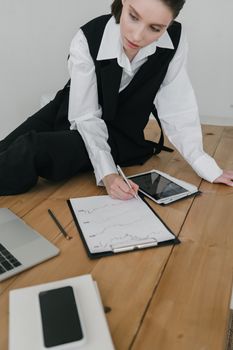 Professional woman in formal attire reviewing charts on a clipboard in a modern office.