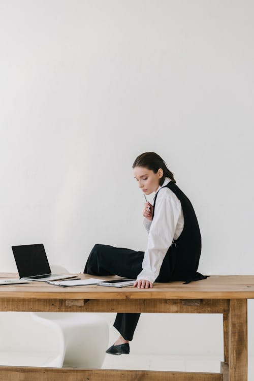 A Woman Sitting on a Wooden Table Near a Laptop