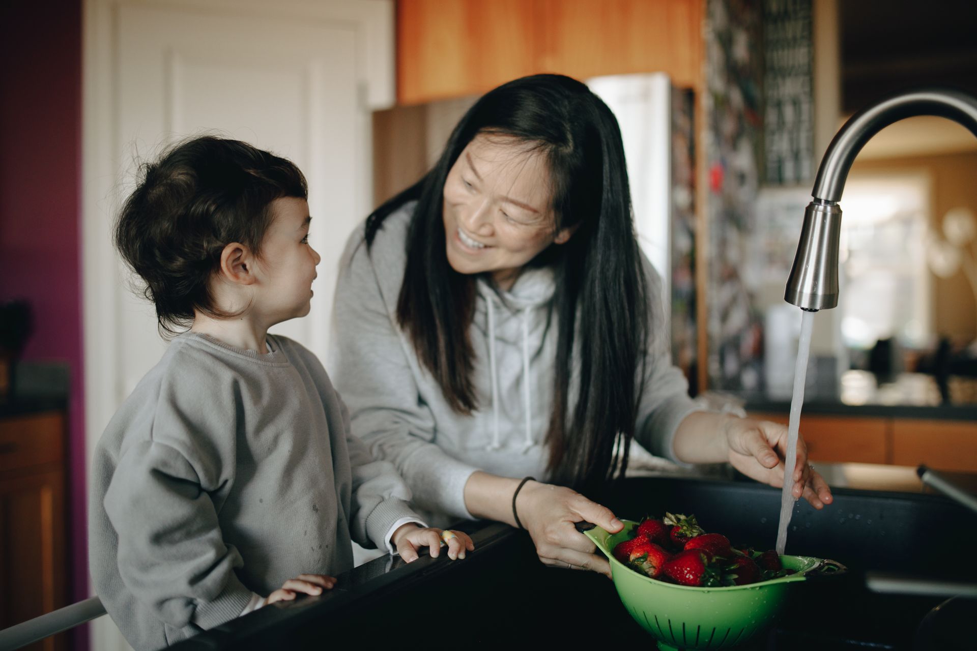 A joyful mother and child enjoying quality time washing strawberries in a modern kitchen.