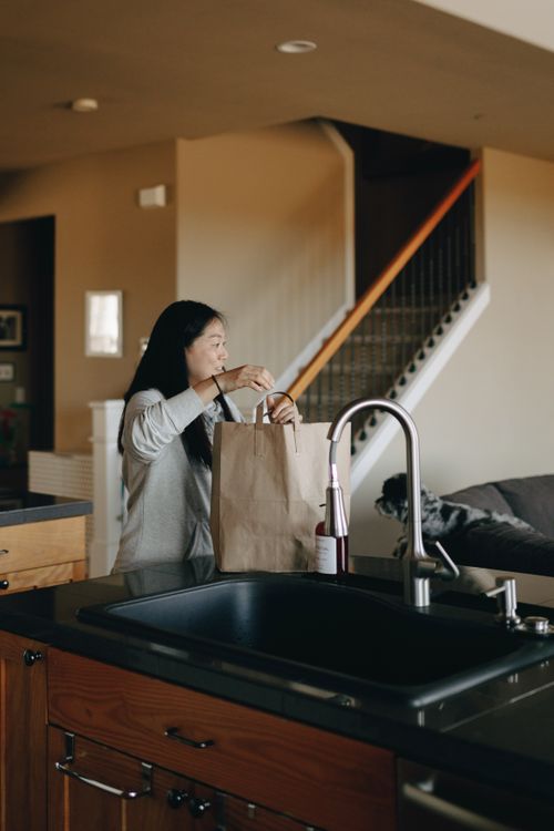 Free Asian woman unpacking groceries in a stylish kitchen, creating a cozy home atmosphere. Stock Photo