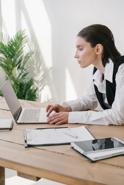 Businesswoman using laptop in modern office space with documents and technology.