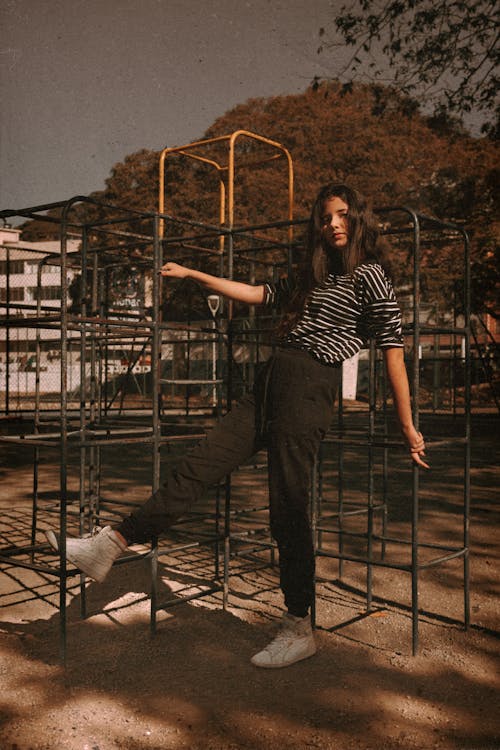 A Woman in Black Pants and Striped Shirt Standing on the Playground