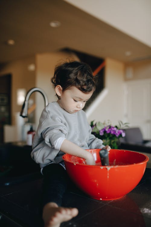 Baby sitting on kitchen counter with strainer on his head Stock Photo