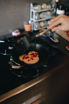 Close-up of cooking pancakes with berries in a kitchen setting.