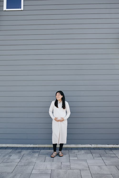 Pregnant Woman Standing Beside A Gray Wall