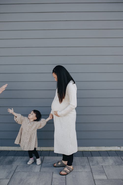 Mother And Child Standing Beside A Gray Wall