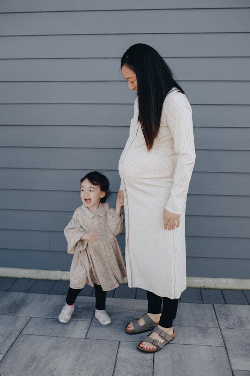 Mother And Daughter Standing Near A Gray Wall