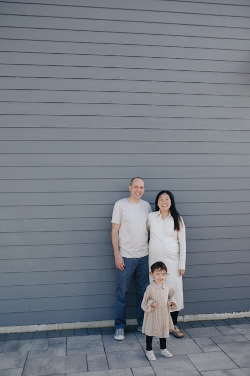 Couple And Their Daughter Standing Near A Gray Wall