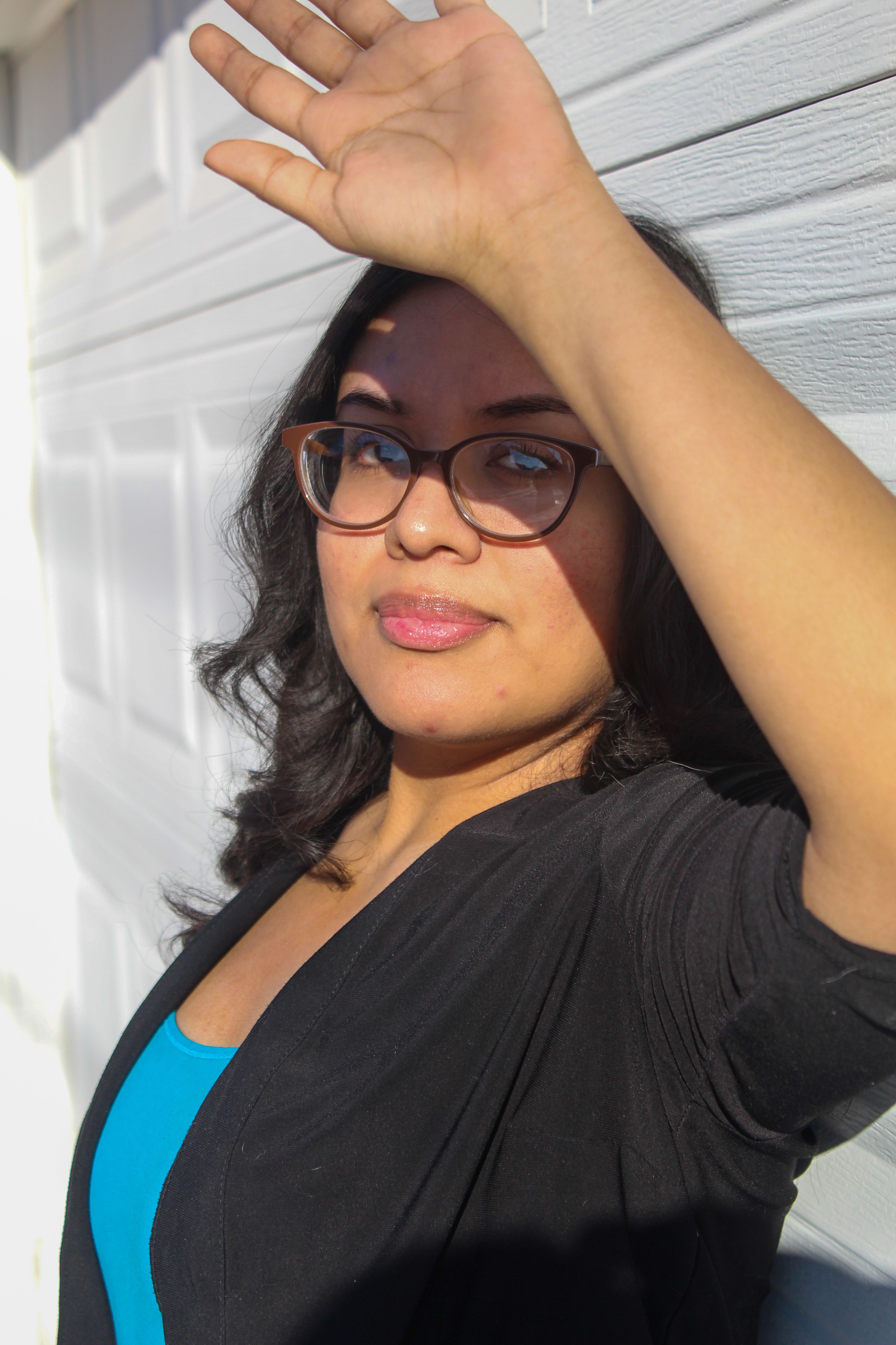 A woman in eyeglasses raising her arm to block sunlight outdoors.