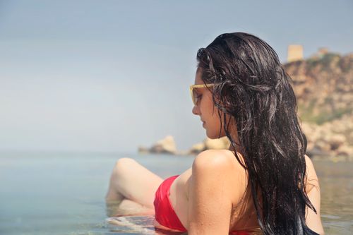 Free Young woman in a red bikini relaxing by the sea, enjoying a sunny day. Stock Photo