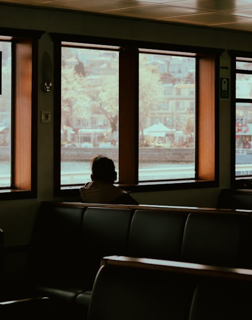 Back view of anonymous male resting and admiring city in window of cruise ship while sailing