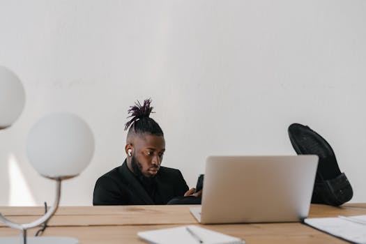 African American businessman in a modern office, multitasking with a laptop and smartphone.
