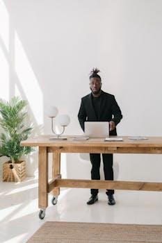 Businessman standing at a desk with a laptop in a bright modern office.