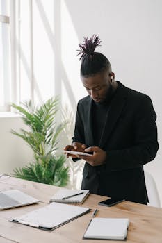 Black man in suit using smartphone in a bright office with plants.