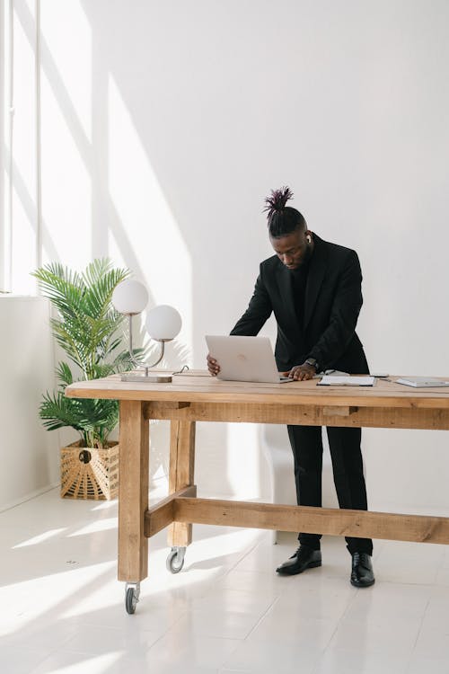 Man in Black Suit Standing while using Laptop