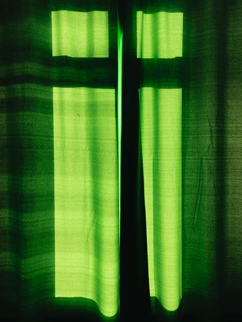 Shadow of window on green curtains hanging in light room on sunny day