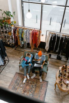 Two adults sitting on a sofa browsing in a fashion boutique with racks of colorful clothes around.