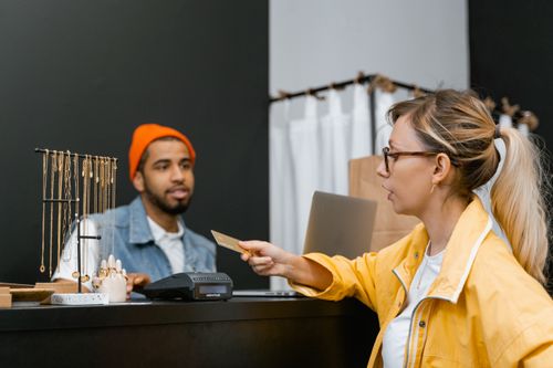 Free Woman in yellow jacket pays with credit card at shop counter with jewelry display. Stock Photo