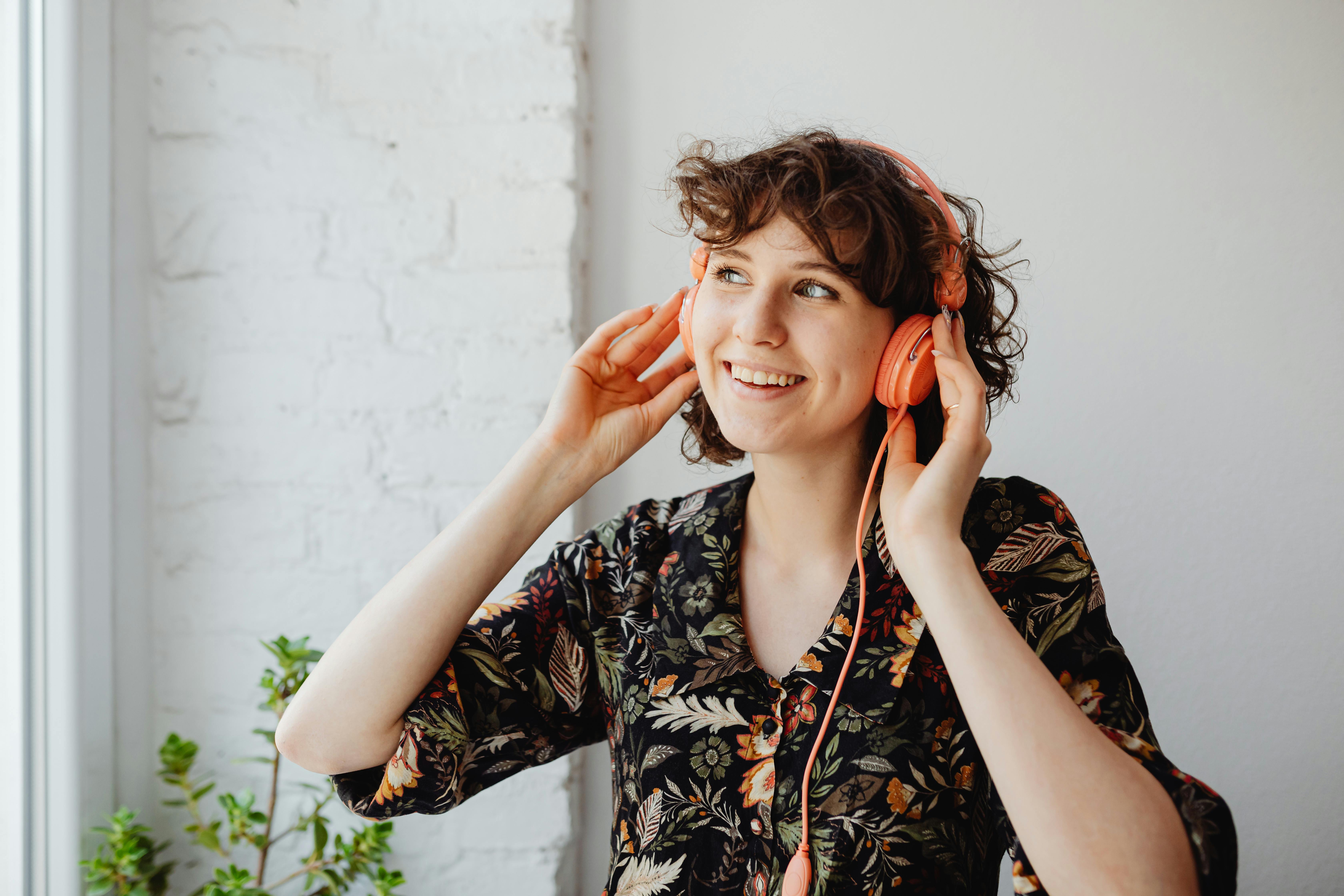 Smiling woman wearing headphones and floral dress enjoying music indoors.