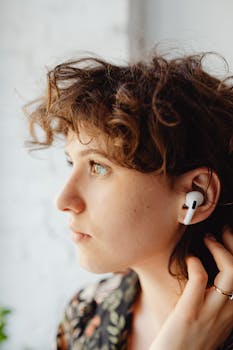 Close-up of a young woman with curly hair wearing wireless earbuds indoors.