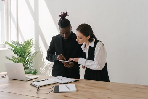 Free A modern business setting with two professionals reviewing a tablet at a desk. Stock Photo