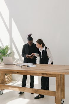 Two business professionals collaborating over a table with documents and a laptop in a bright office.