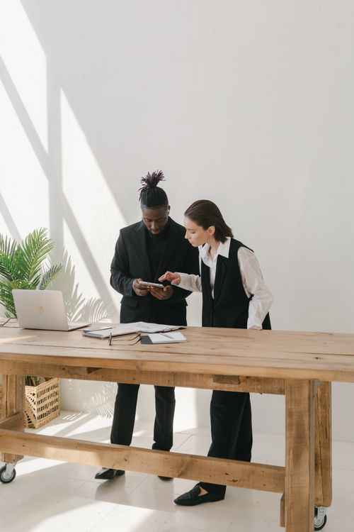 Free Two business professionals collaborating over a table with documents and a laptop in a bright office. Stock Photo