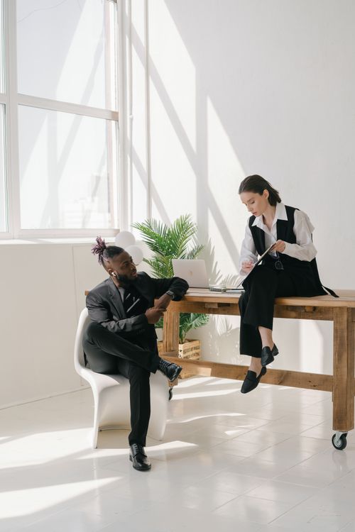 Free Two colleagues discuss work in a bright office setting with natural light. Stock Photo
