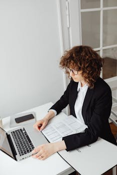 A focused businesswoman with curly hair using a laptop at her home office desk.