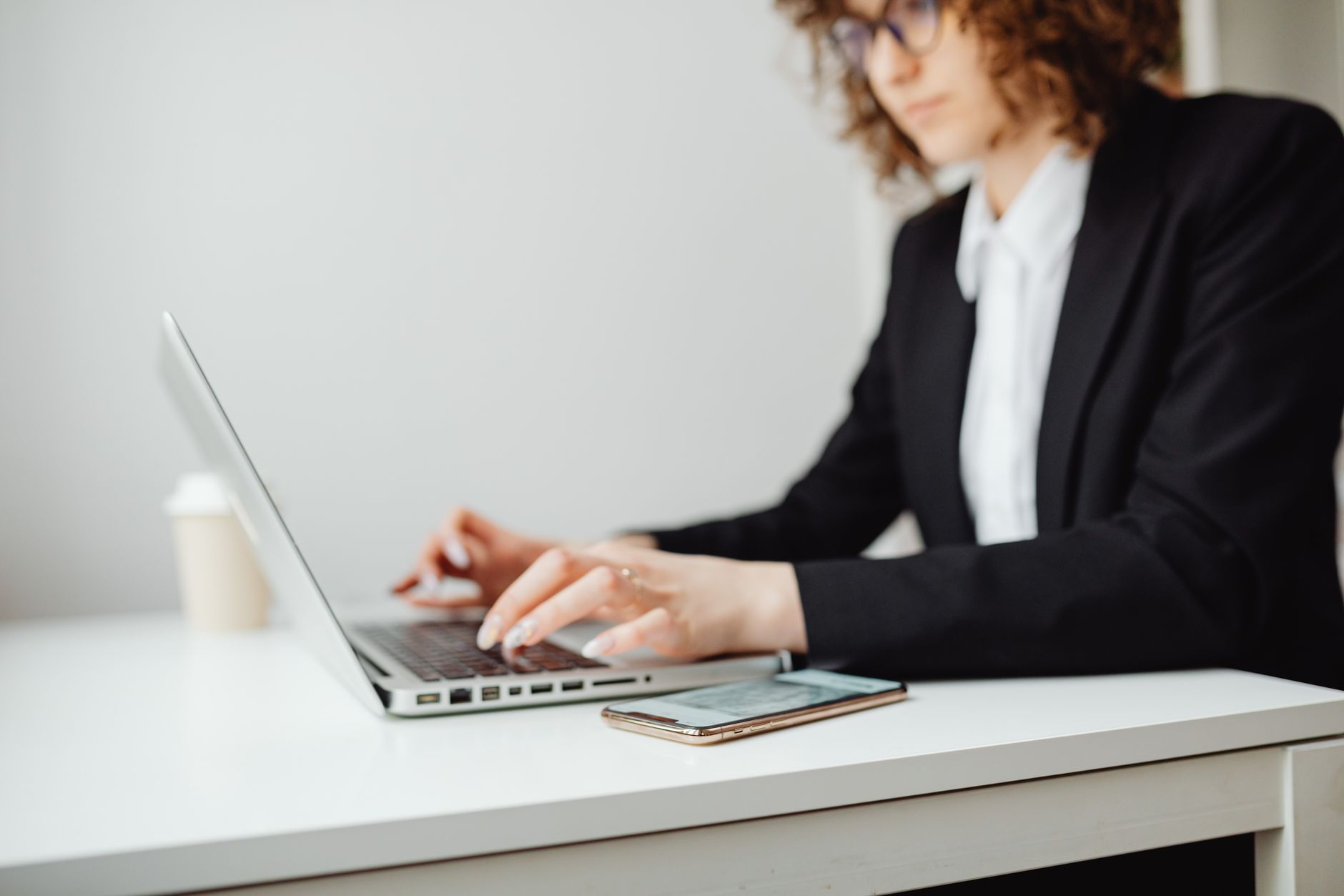 A woman at a desk with an open laptop, typing a message on her smartphone