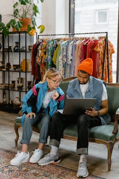 African American man and Caucasian woman discussing a project on a laptop in a fashion studio.