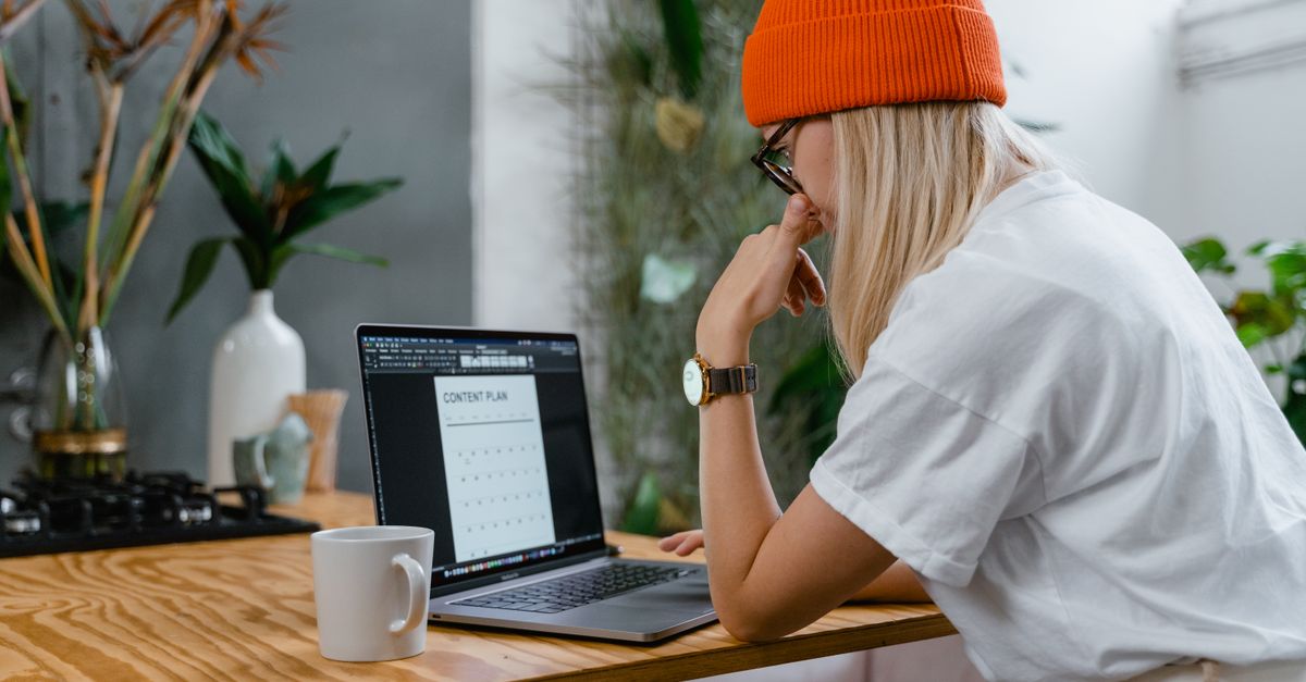 person working on laptop in a cozy home office with a coffee mug and a vision board