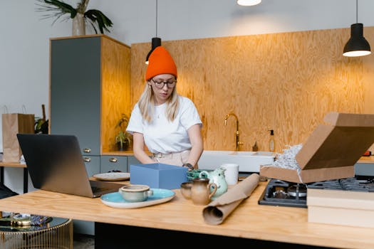 Young woman packaging handmade ceramics in a modern kitchen for her online business. Warm interior setting.