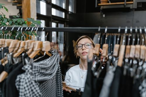 Free A woman with glasses browsing clothes in a fashion boutique, exploring various styles. Stock Photo