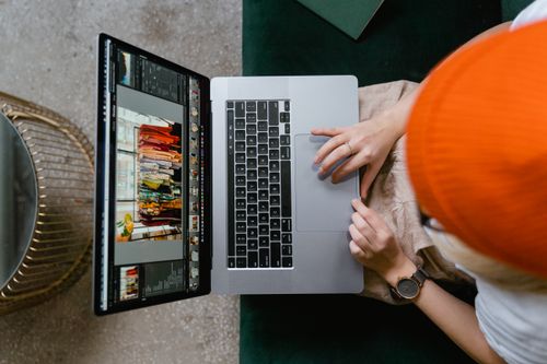 Free Person wearing orange beanie editing photos on laptop using professional software. Stock Photo