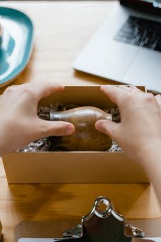 Person packaging a ceramic pot into a cardboard box on a wooden table.