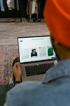 Adult man browsing clothing options on a laptop in a cozy indoor setting.