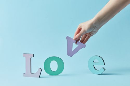 Free A hand arranging the word 'Love' with colorful letters against a pastel blue backdrop. Stock Photo