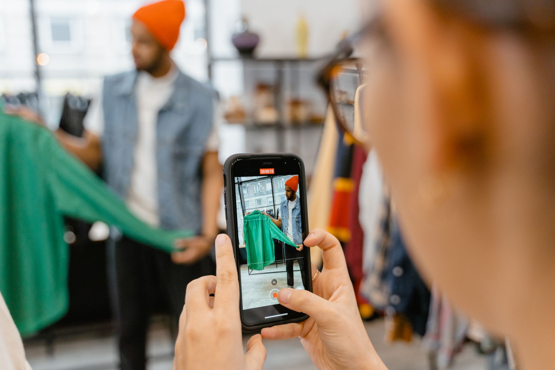 Person taking a picture of a green jacket using a smartphone in a clothing shop.