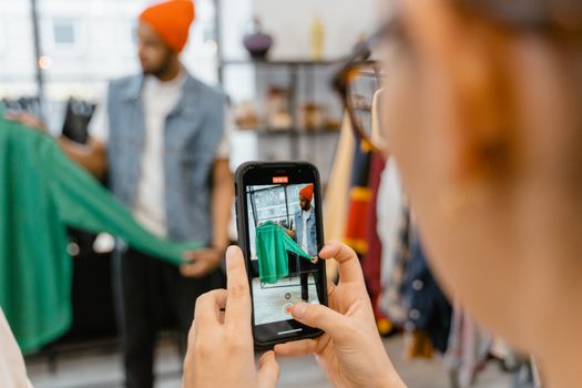 Person taking a picture of a green jacket using a smartphone in a clothing shop.