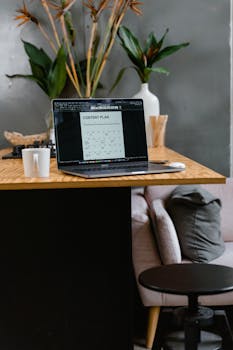 Stylish home office table with laptop, ceramic mug, and plants creating a productive workspace.