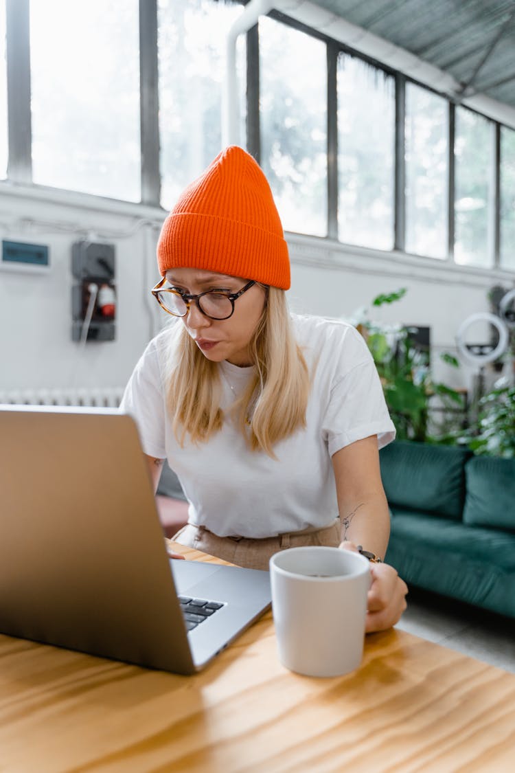 A Woman In An Orange Bonnet Using Her Laptop While Having Coffee