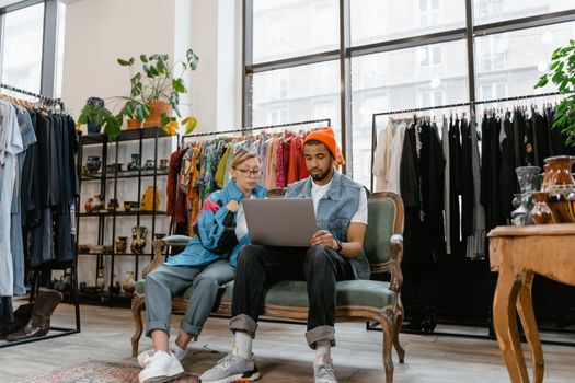 A man and woman collaborating on a laptop in a stylish vintage shop with clothes in the background.