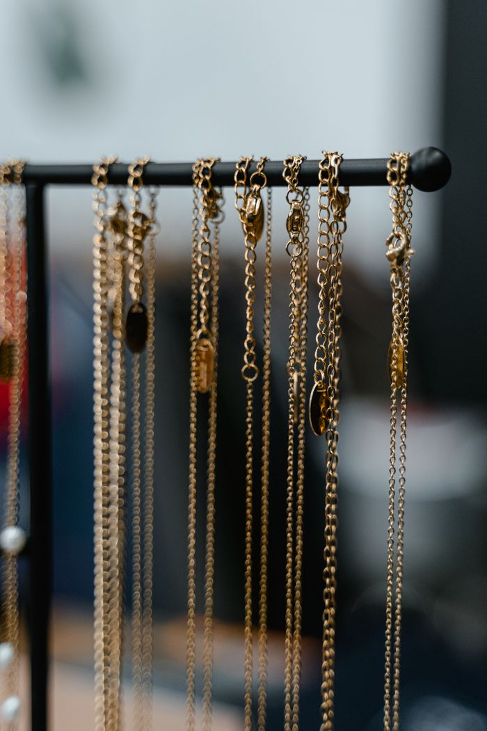 A dozen fine gold chains with small pendants hanging from a black display rack