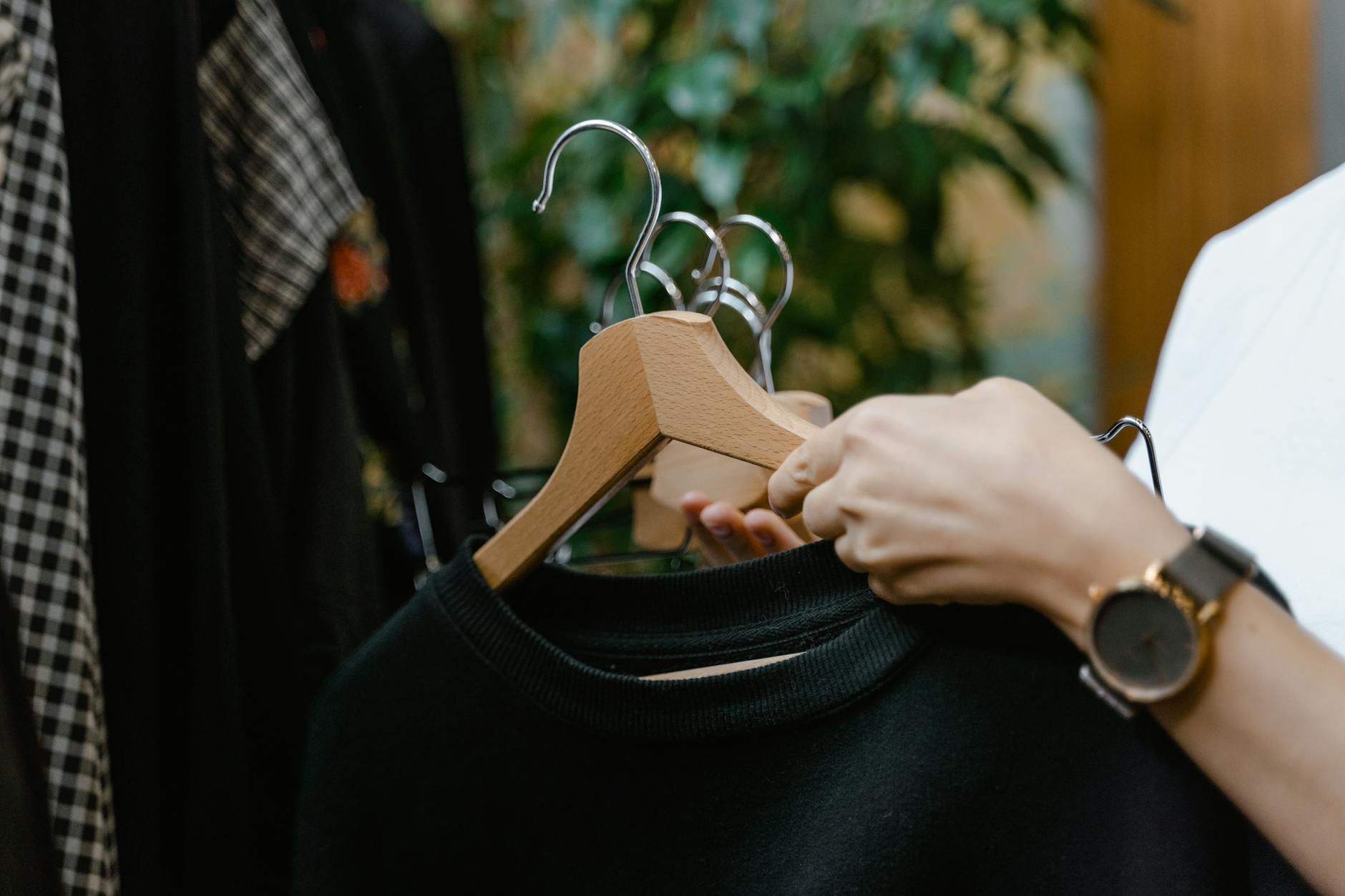 Close-up of hands holding clothes hangers in a fashion boutique setting.