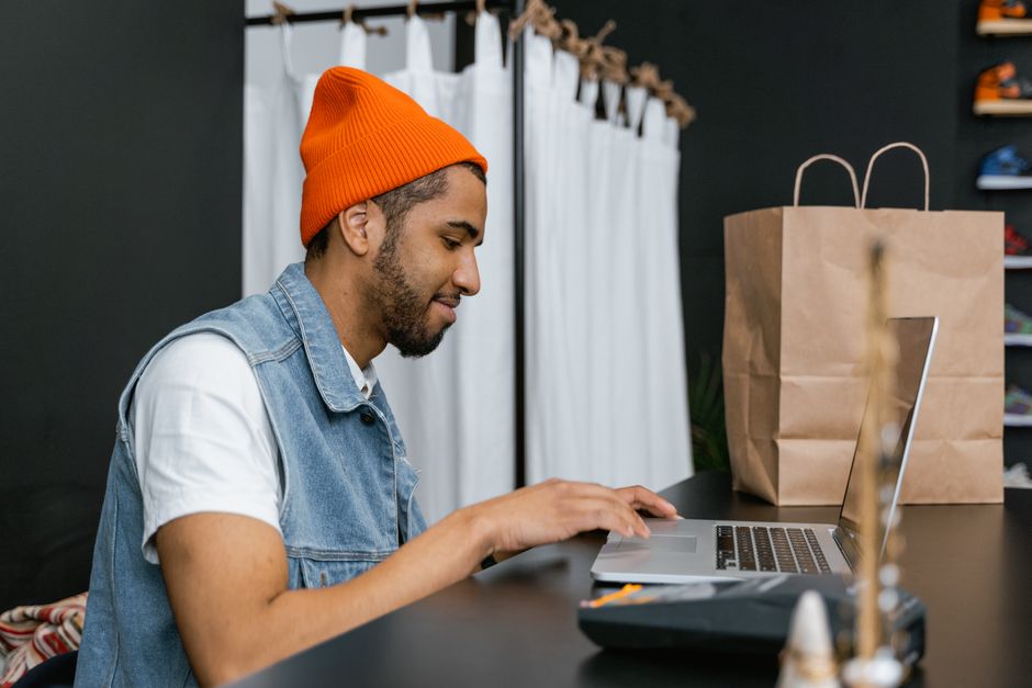 Man in a beanie using laptop in a stylish fashion store, indoors. Man in a beanie using laptop in a stylish fashion store, indoors.